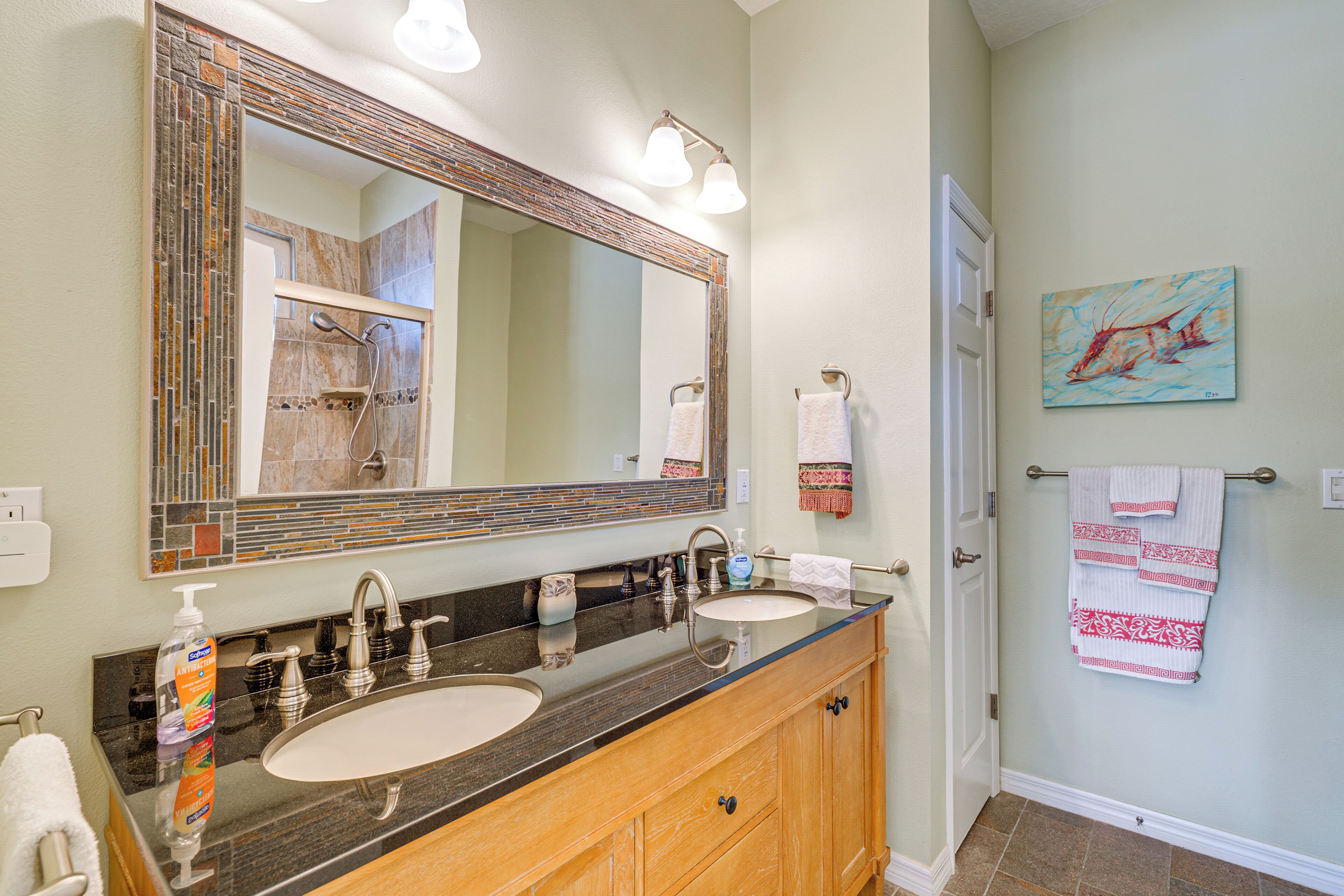 A bathroom with a large mirror, two sinks, a towel rack, and a painting on the wall.