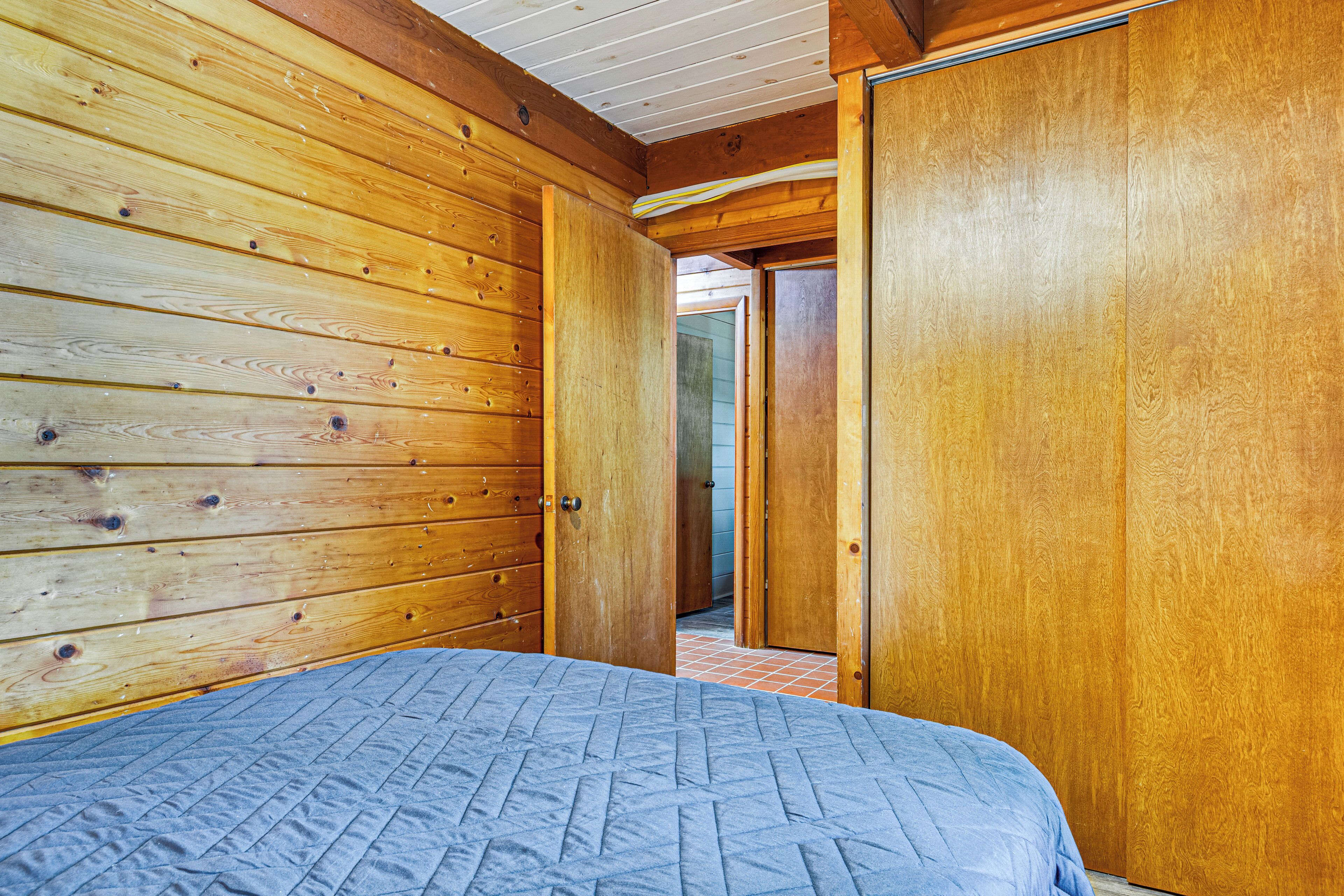 Una habitación con paneles de madera, una cama, una puerta y un pasillo visible.