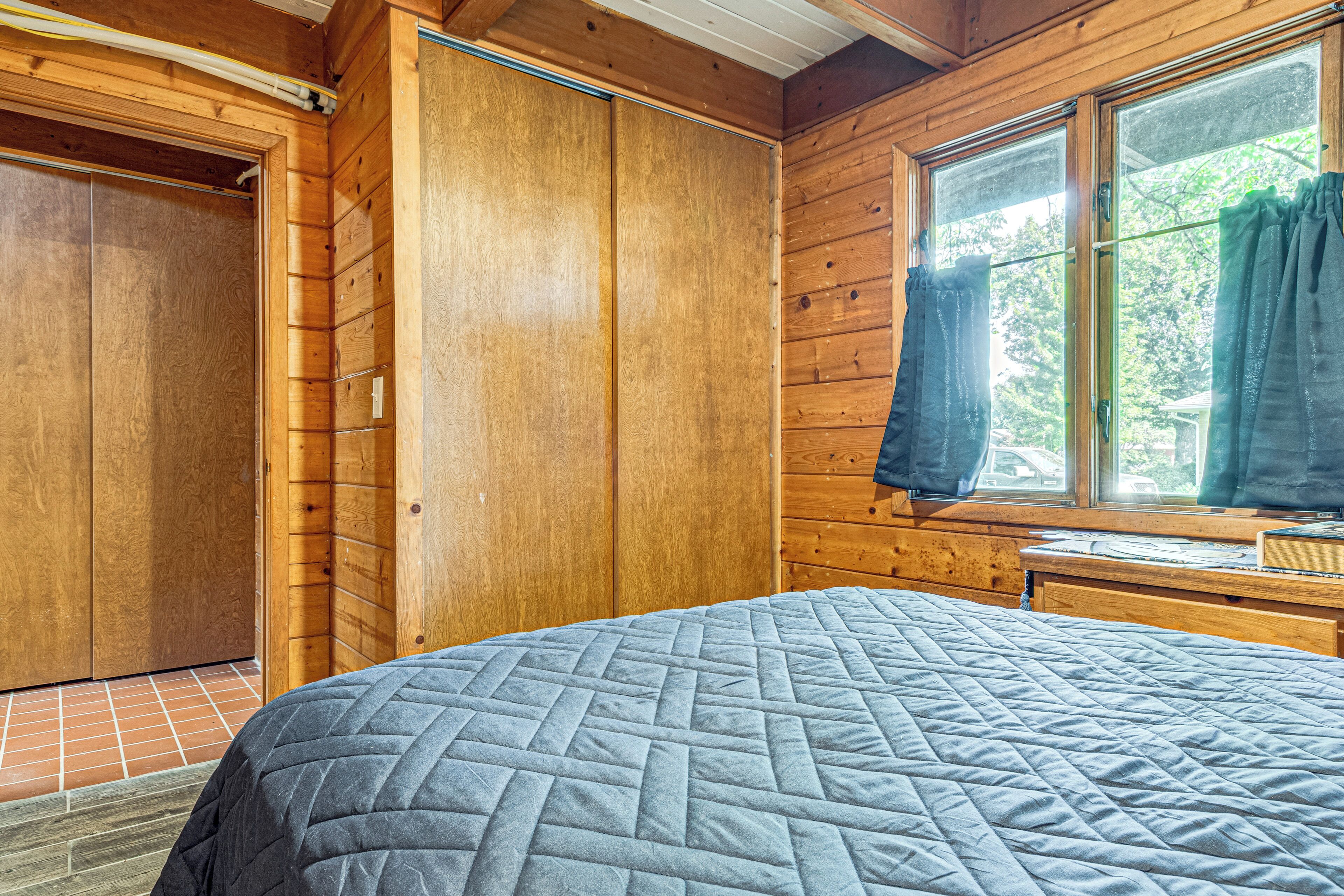 Une chambre dans une cabane en bois, avec un lit, une fenêtre avec des rideaux et une porte.