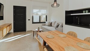 A modern kitchen with a black countertop, a wooden dining table with woven placemats, a sofa, and a hanging light fixture. - Elsa Modern Apartments (Pogonia)