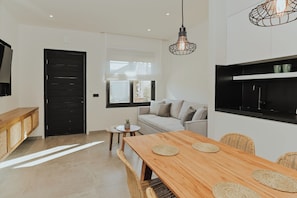 Una cocina moderna con encimera negra, una mesa de comedor de madera con individuales tejidos, un sofá y una lámpara colgante.