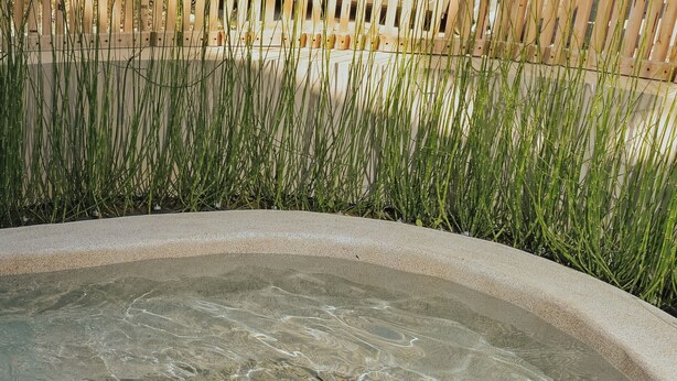 A hot tub with clear water, surrounded by a wooden deck and tall grass. - Elsa Modern Apartments (Pogonia)