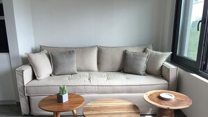 A modern living room with a sofa, two wooden tables, and a small potted plant. - Elsa Modern Apartments (Pogonia)