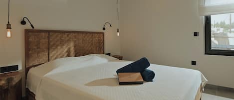 Een netjes opgemaakt bed met een houten hoofdbord, nachtkastje, lamp en een raam met uitzicht.