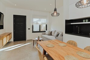 A modern kitchen with a black countertop, a wooden dining table with woven placemats, a sofa, and a hanging light fixture.
