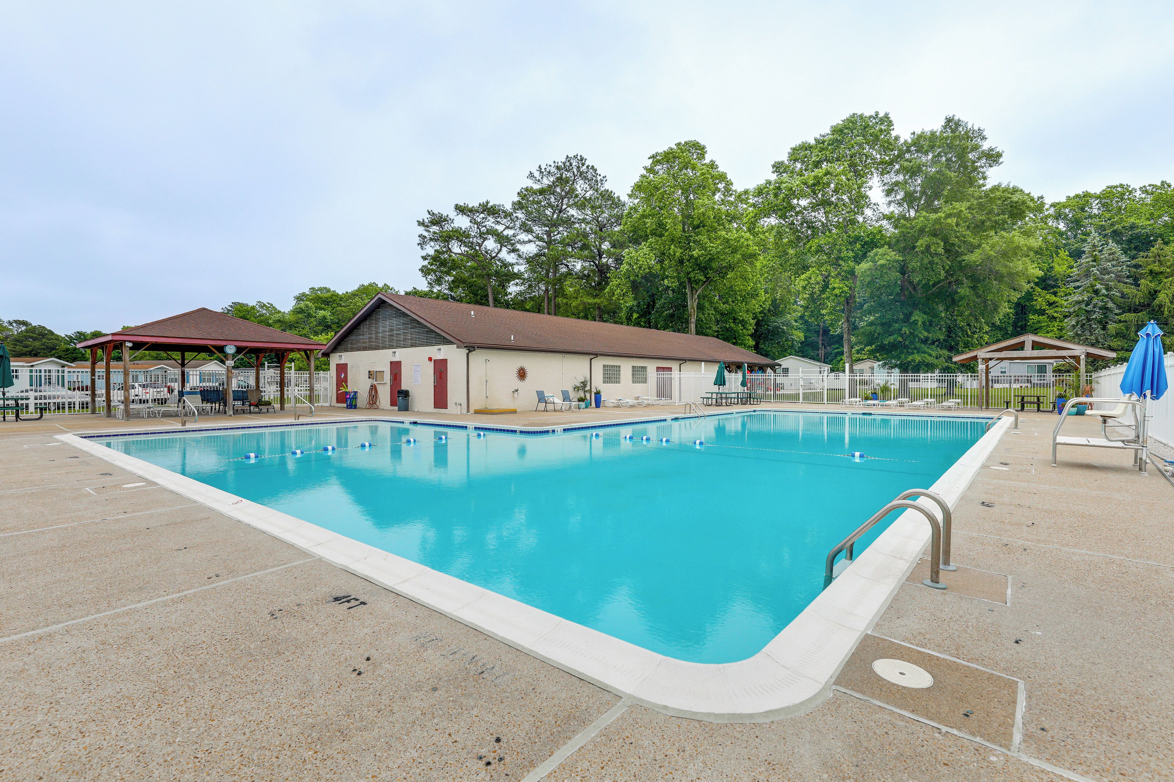 A swimming pool with a covered area and lounge chairs, surrounded by a fence and trees.