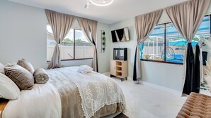 Ein Schlafzimmer mit einem Bett, Vorhängen, einem Fernseher, einem Holzschrank und Blick ins Freie.