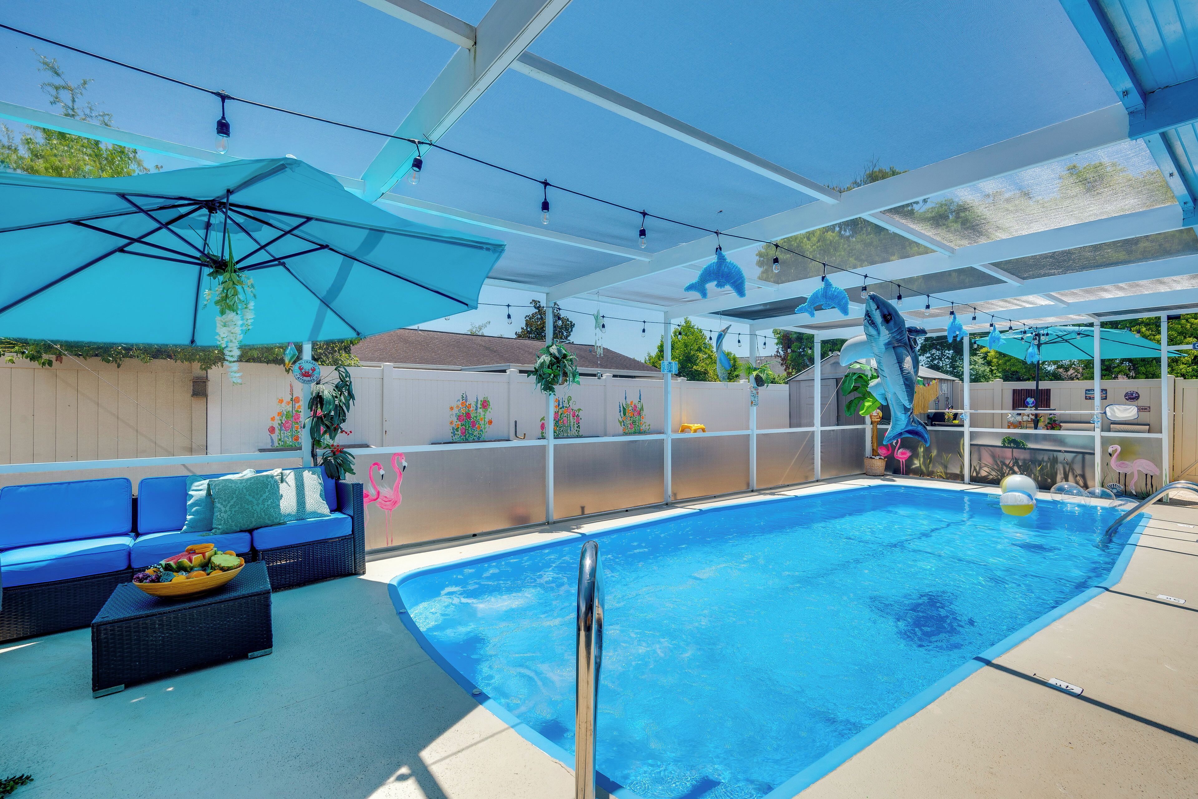 Una piscina amb un parasol blau, un sofà blau i una taula petita amb fruita.