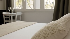 Ein Hotelzimmer mit Bett, einem Vorhangfenster, einem Tisch mit Stühlen und Blick auf Gebäude.