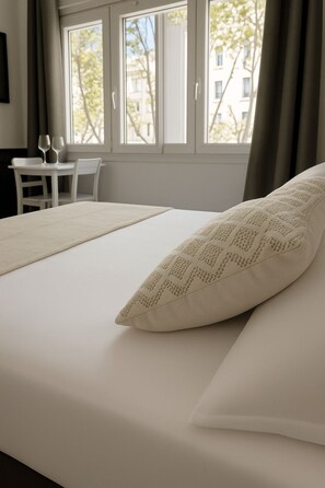 Ein Hotelzimmer mit Bett, einem Vorhangfenster, einem Tisch mit Stühlen und Blick auf Gebäude.