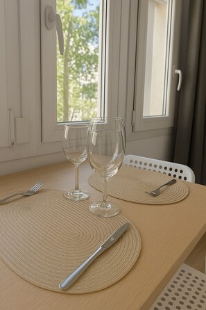 A dining table with two wine glasses, a fork, and a knife on woven placemats, set against a window with curtains. - Comfortable Studio Apartment | La Rambla 113, Downtown, Close to Everything (Cataluña)