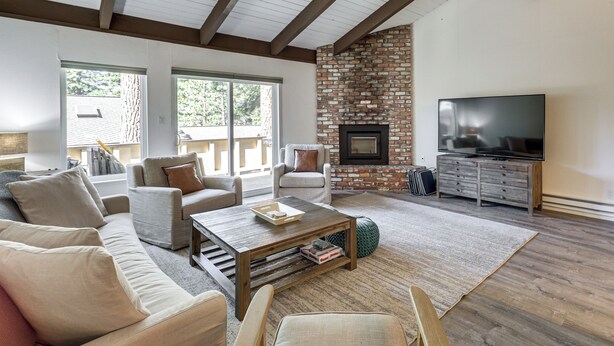 Una sala de estar con chimenea, sofá, mesa de centro, televisor y suelo de madera.