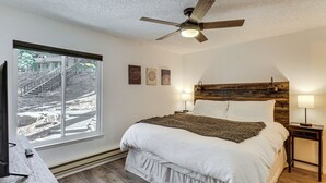 Un dormitorio con cama, ventilador de techo, lámparas de noche, ventana con vista a las escaleras y cabecero de madera.