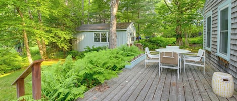 A wooden deck with a table and chairs, surrounded by lush greenery and a small shed.