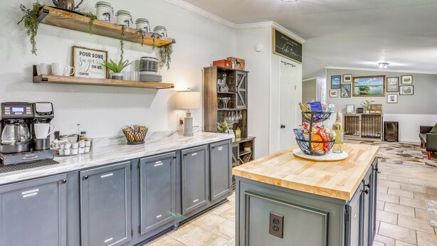Una cocina con armarios grises, encimera de madera, una cafetera y estantes con utensilios de cocina.