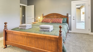 Quarto com cama de madeira, roupa de cama verde e almofada estampada vermelha.