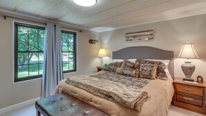 Ett sovrum med en stor säng, en bänk, ett sängbord med en lampa och ett fönster med gardiner.