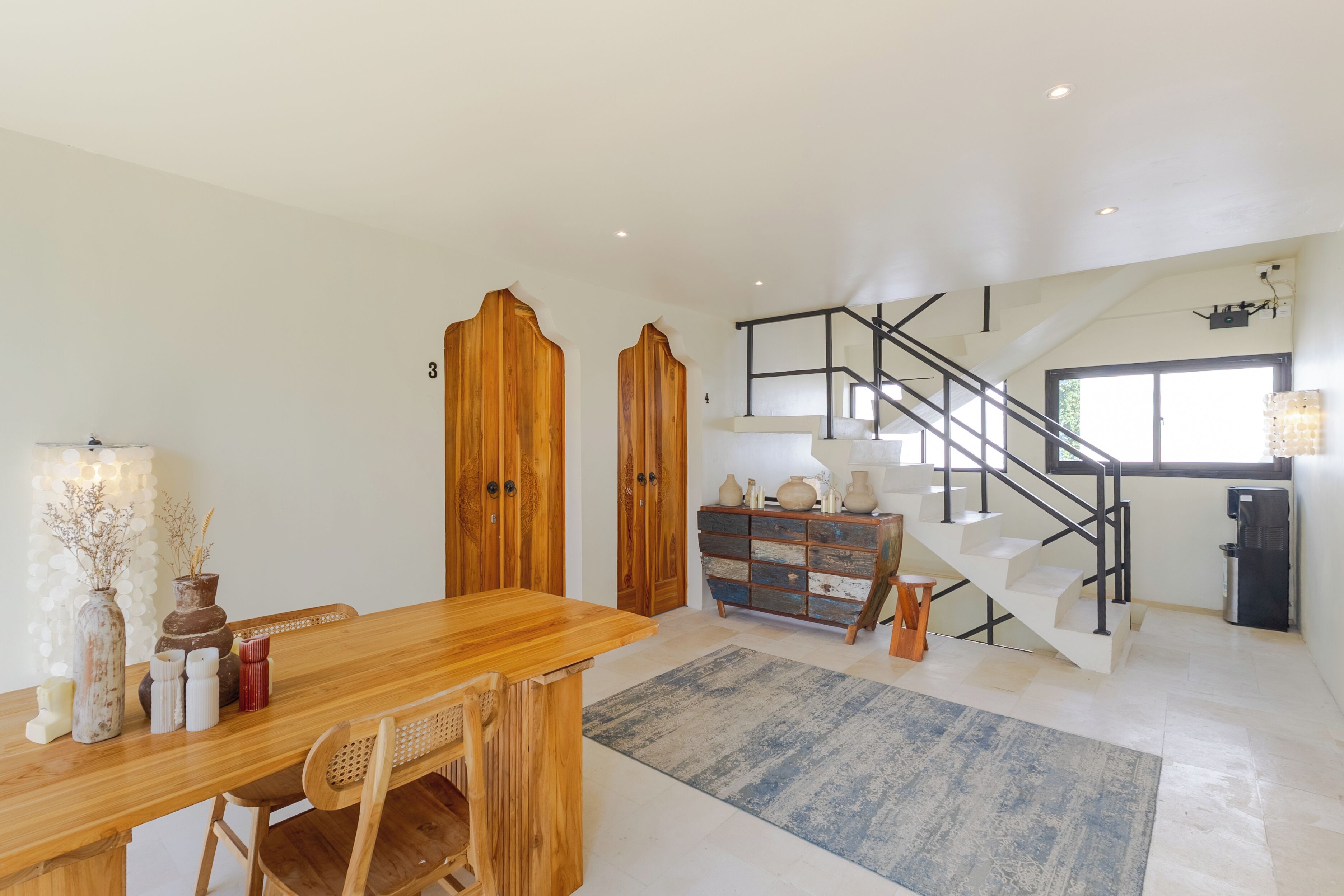 A spacious living area with a wooden dining table, a staircase, and a view of the outdoors.