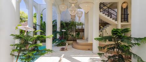 An indoor courtyard with white columns, hanging wicker chandeliers, and potted plants.