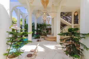 Un patio interior con columnas blancas, lámparas de mimbre colgantes y plantas en macetas.