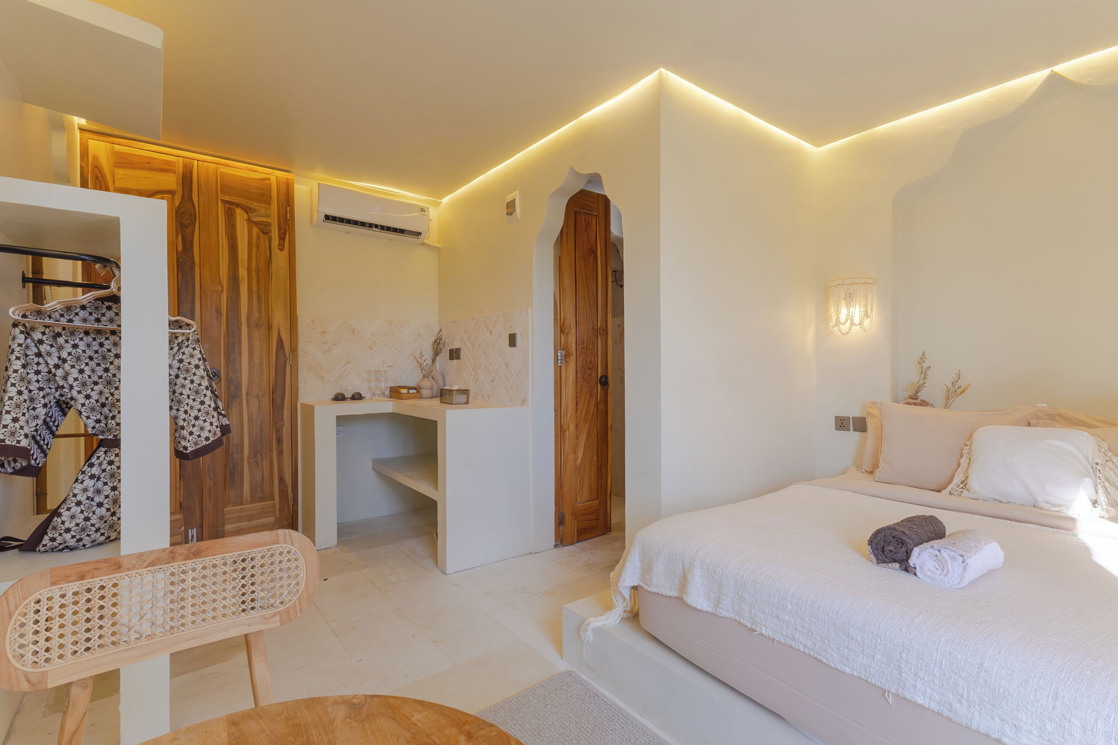 A bedroom with a bed, a wooden wardrobe, a vanity with a mirror, and a hanging robe.