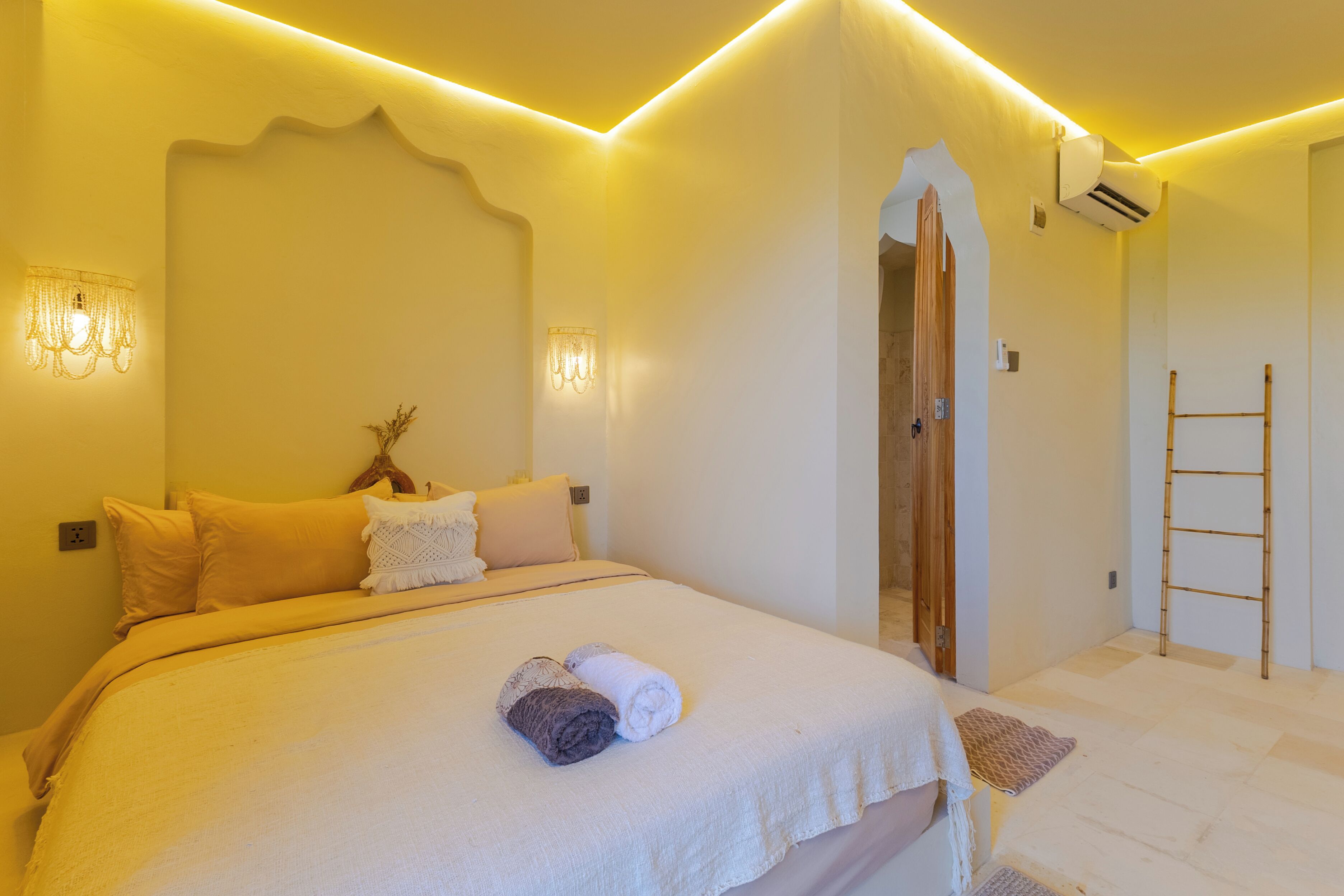 A bedroom with a bed, pillows, a wall-mounted air conditioner, and a wooden ladder.