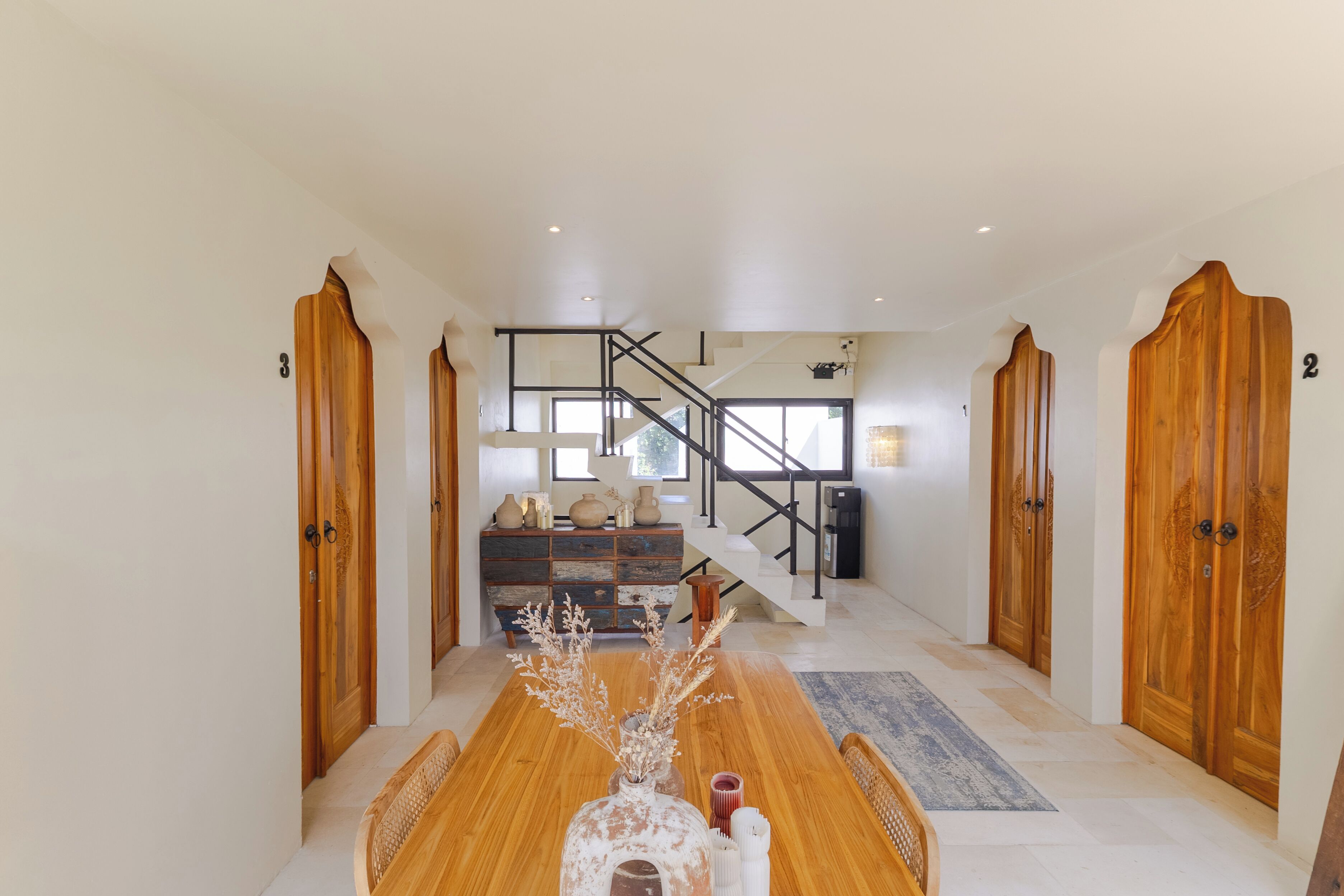 A spacious dining area with a wooden table, a staircase, and wooden doors.