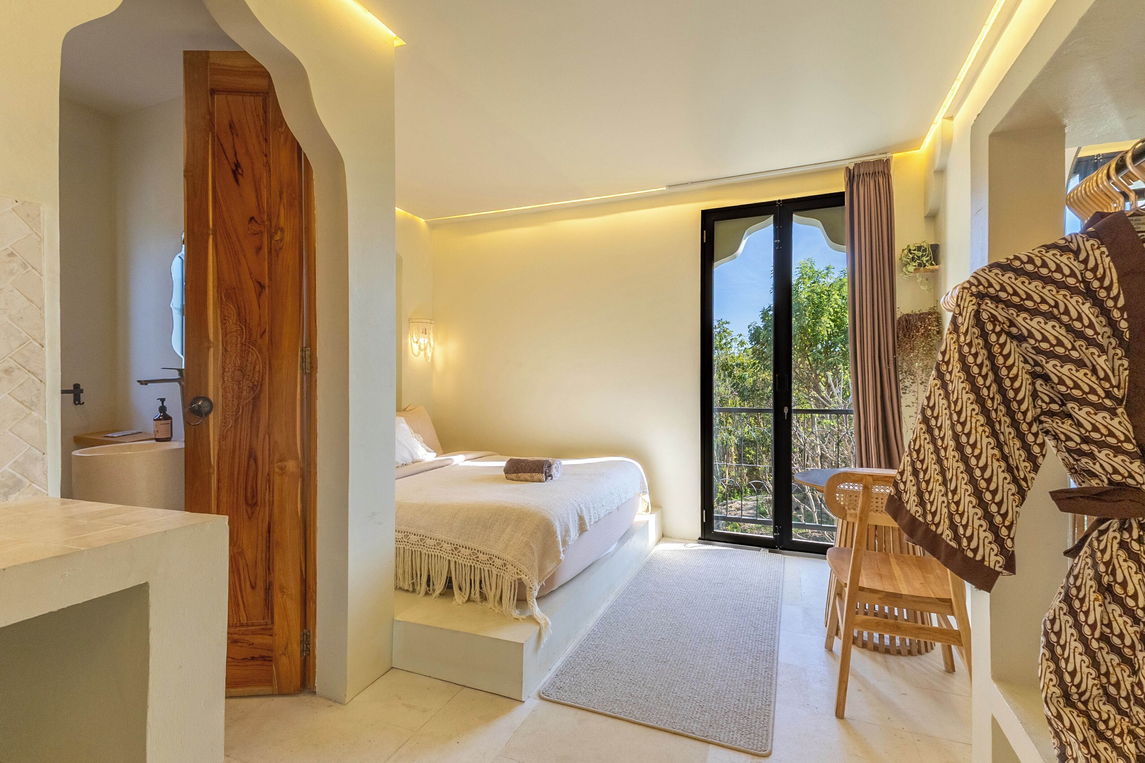 A bedroom with a bed, a wooden door, a bathroom, and a balcony with a view.