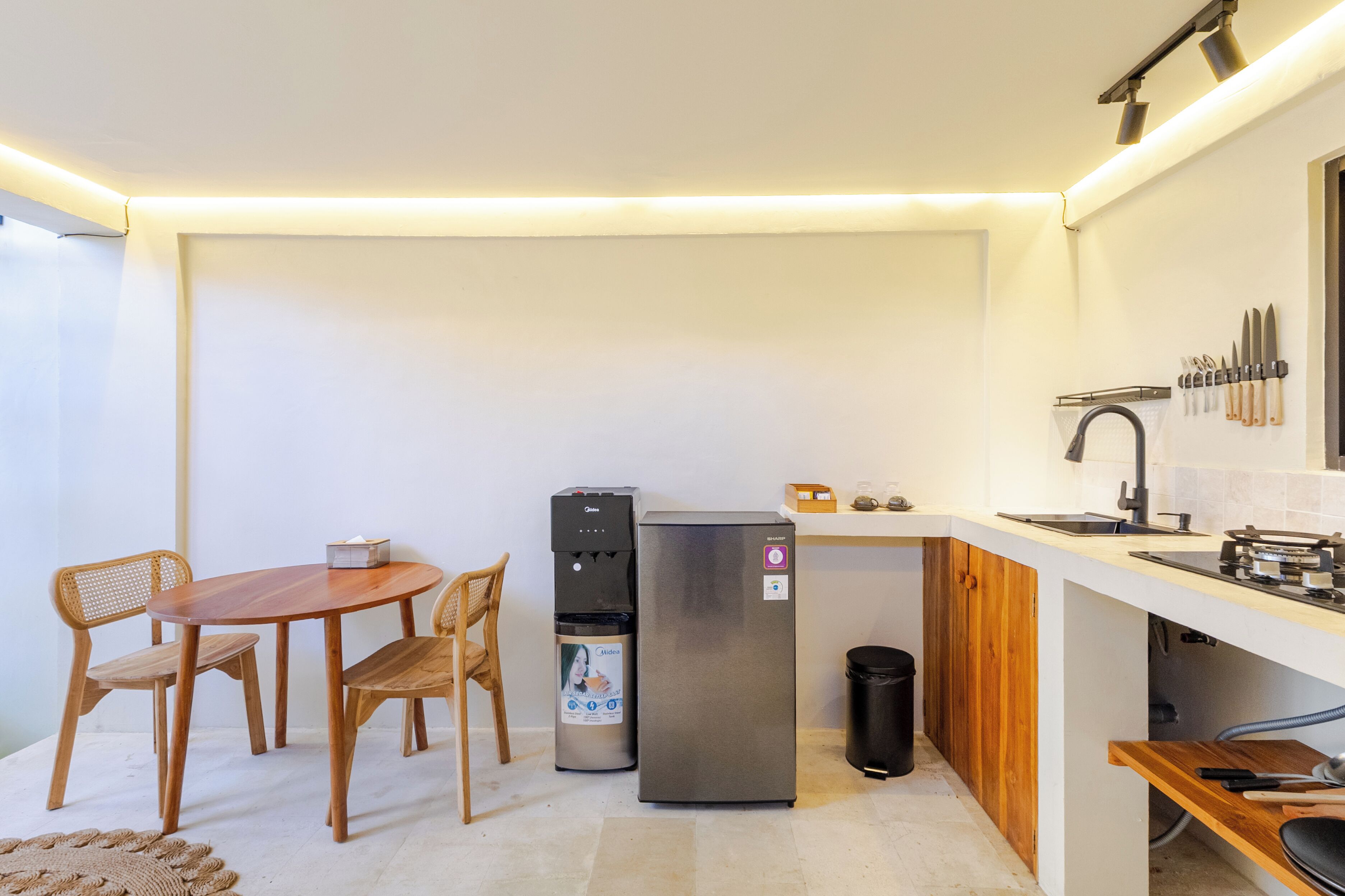 Eine kleine Küche mit Kühlschrank, Wasserspender und einem Holzespeisetisch mit Stühlen.