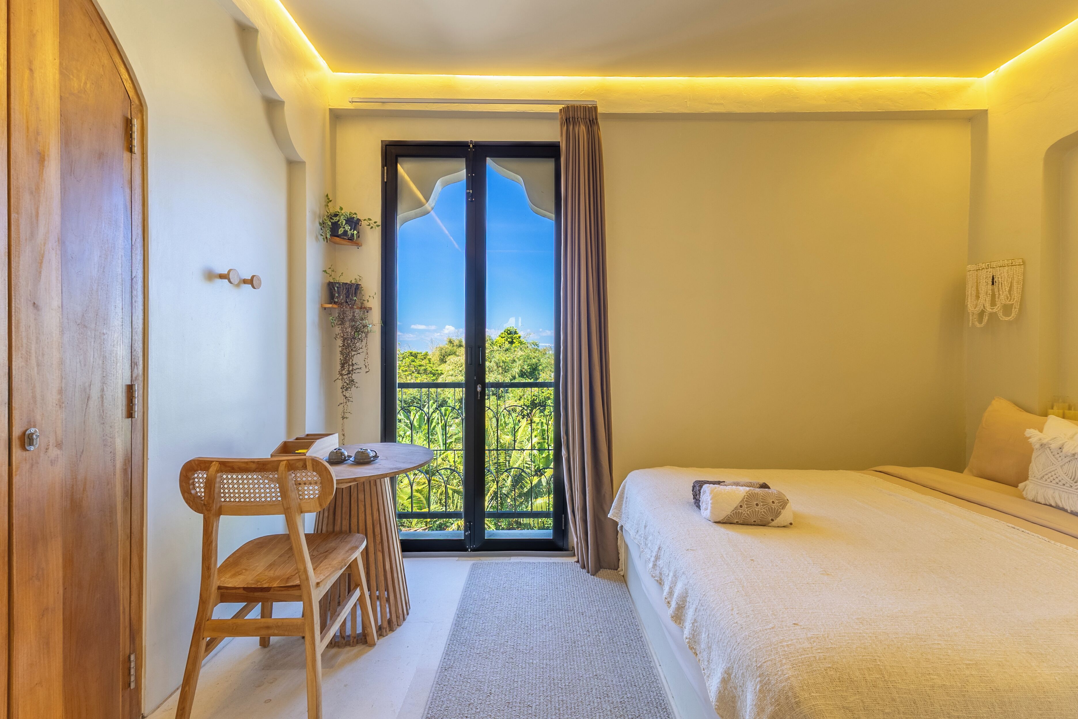 Una camera da letto con un letto, una sedia di legno, un tavolo, vista attraverso una porta vetrata e una lampada a soffitto.