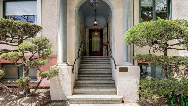 Fachada de edificio con escaleras, columnas y una lámpara colgante.