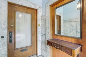 Eine Holztür mit Glasfenster, eine Marmorwand und ein Holzanfangstisch mit Spiegel.