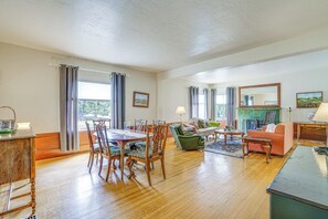 Ein geräumiges Wohnzimmer mit Essbereich, Holzboden und großen Fenstern mit Vorhängen.
