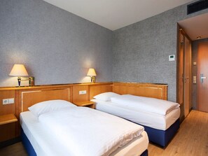 Een hotelkamer met twee enkele bedden, houten hoofdeinden, nachtkastjes met lampen en een houten vloer.