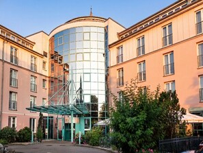 Ein Hotel mit moderner Glasfassade, einer überdachten Eingangspartei und einem Innenhof mit Grünflächen.