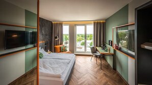 Una habitación de hotel moderna con una cama grande, un escritorio, un televisor y vistas al exterior.