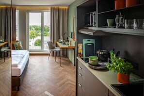 Une chambre d’hôtel équipée d’un lit, d’un bureau, d’une chaise, d’une kitchenette et de grandes fenêtres.
