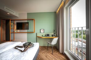 Ein Hotelzimmer mit einem Bett, einem Schreibtisch mit Stuhl, einem Fernseher und einem Fenster mit Blick.
