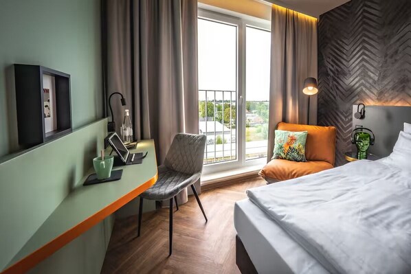 Ein Hotelzimmer mit Bett, Schreibtisch mit Stuhl, einem Fenster mit Vorhängen und Blick ins Freie.