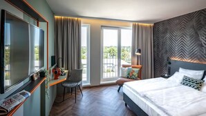 Quarto de hotel com cama, mesa com televisão, cadeira e varanda com cortinas.