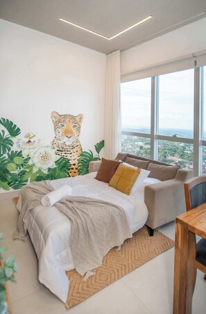 Camera da letto con un'ampia finestra, un letto, un divano e un quadro che raffigura un leopardo.
