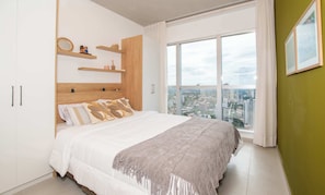 Un dormitorio con una cama grande, cabecera de madera y vista a la ciudad a través de un ventanal.