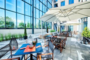 Ein Terrassenbereich im Freien mit Tischen, Stühlen, großen Sonnenschirmen und Topfpflanzen.