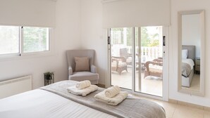 Ein Schlafzimmer mit Bett, Deckenventilator, Stuhl und Blick auf eine Außenveranda.
