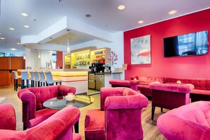 Ein stilvoller Lounge-Bereich mit roten Sofas, einer Bar mit Getränkeauswahl und einem an der Wand befestigten Flachbildfernseher.