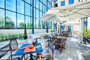Ein Terrassenbereich im Freien mit Tischen, Stühlen, großen Sonnenschirmen und Topfpflanzen.