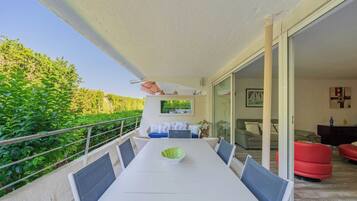 Un balcon avec une table à manger, des chaises et un saladier vert.