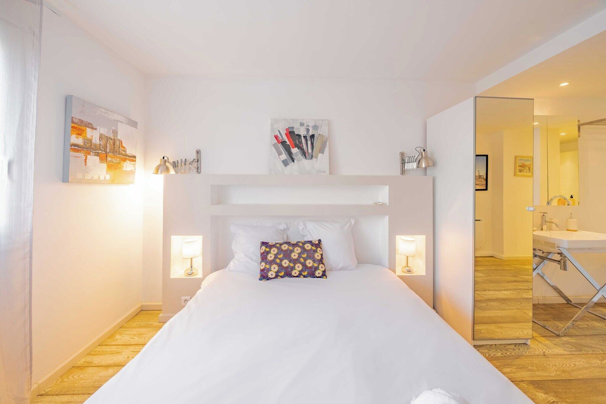 Une chambre d’hôtel avec un lit, des lampes de chevet, un miroir et une salle de bain visible à travers une porte ouverte.