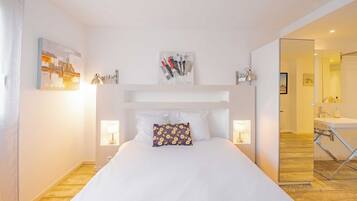 Une chambre d’hôtel avec un lit, des lampes de chevet, un miroir et une salle de bain visible à travers une porte ouverte.