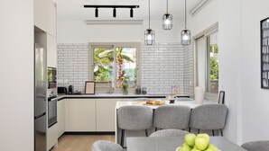 Een moderne keuken met witte kasten, een eethoek met grijze stoelen en uitzicht op groen.